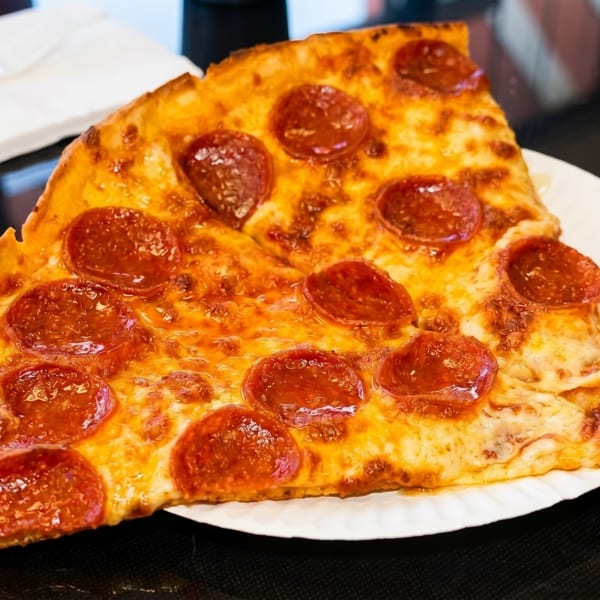Two large slices of pepperoni pizza on a white paper plate, with napkins in the background.