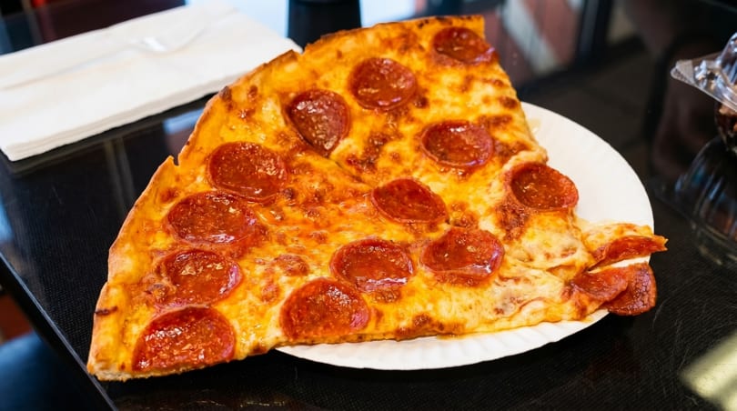 Two large slices of pepperoni pizza on a white paper plate, with napkins in the background.